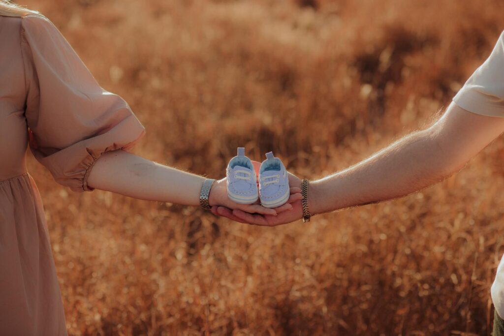 Mother and father holding a pair of blue baby shoes. They are in a golden field together.