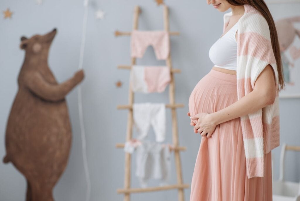 A pregnant woman holding her belly while standing in the nursery prepared for her unborn baby.